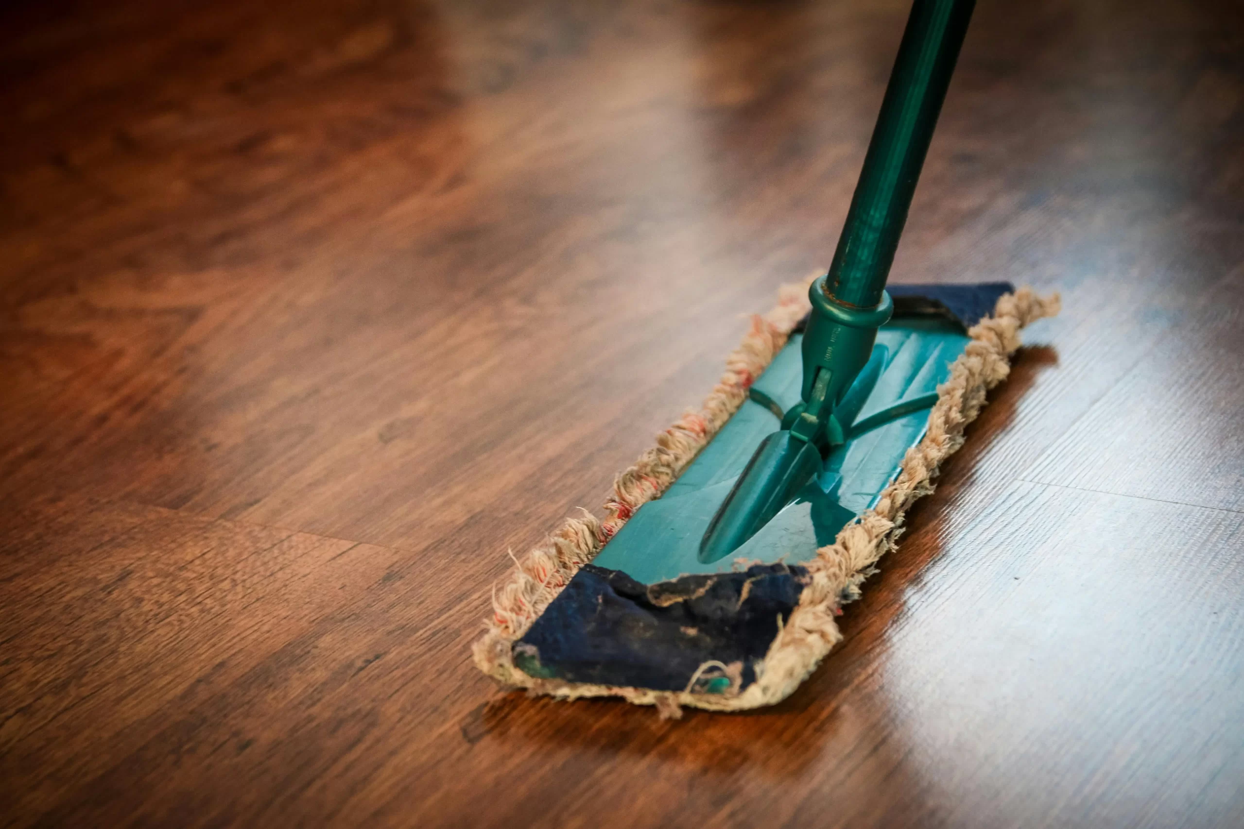Detailní záběr na mop čistící dřevěnou podlahu, ilustrující proces úklidu.